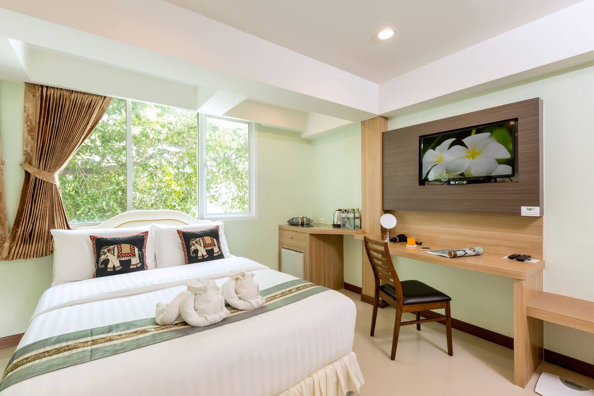 Habitación de hotel con una cama grande, un escritorio, una silla, un televisor y una ventana con cortinas.