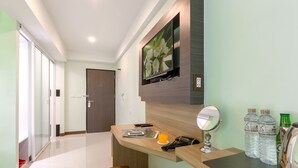 Habitación de hotel con una encimera de madera, un espejo grande, un televisor de pantalla plana en la pared y una puerta que da a otra habitación.