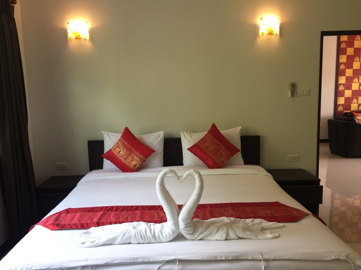 A hotel room with a neatly made bed, two red pillows, and a swan-shaped towel arrangement.