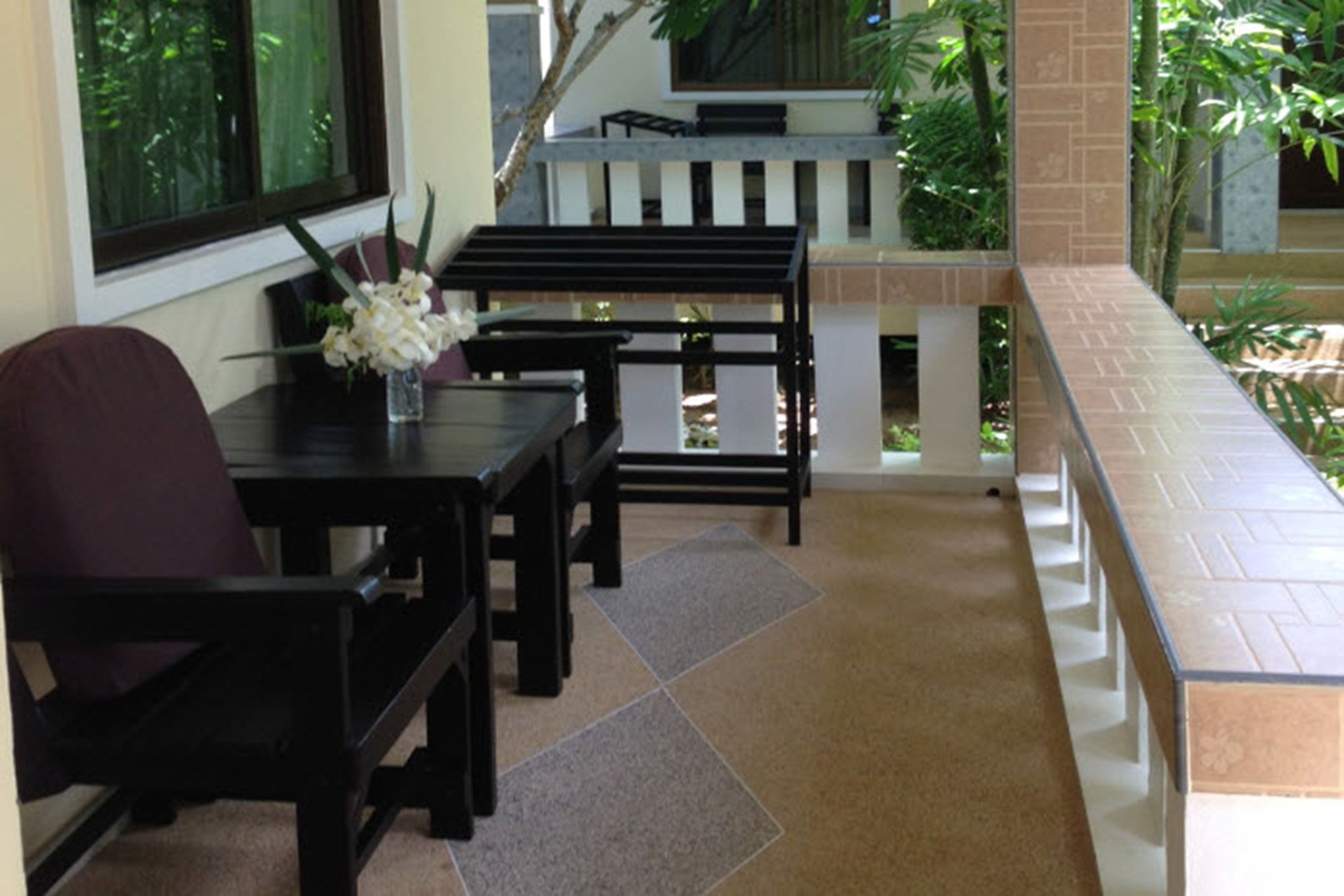 A balcony with a tiled floor, a wooden table with chairs, and a vase with flowers.