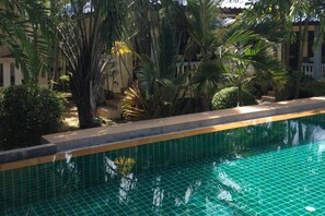 Una piscina con borde de baldosas, rodeada de palmeras y vegetación.