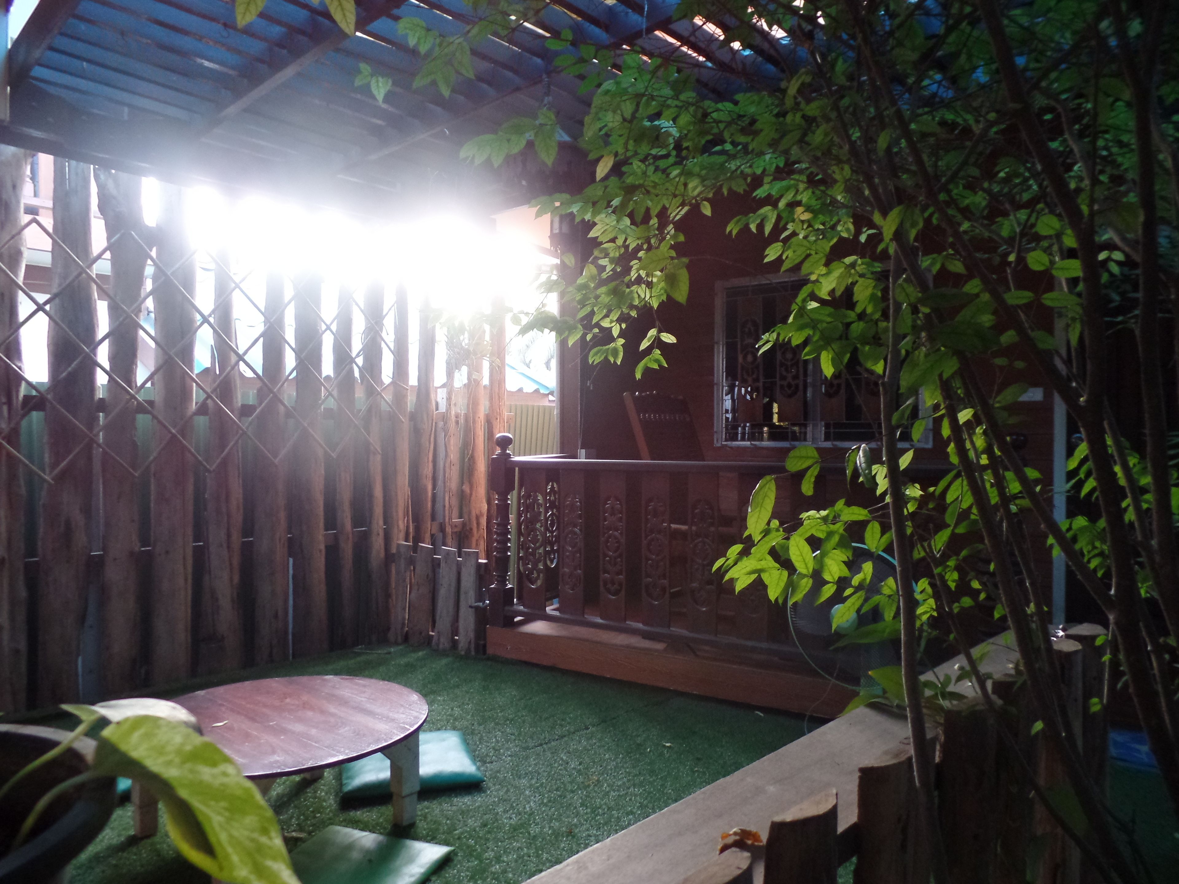 A patio with a wooden table and green cushions, surrounded by a wooden fence and a small garden area.