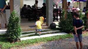 An outdoor dining area with tables and chairs, palm trees, and a covered walkway. - Naya Pool Villa (Rawai)
