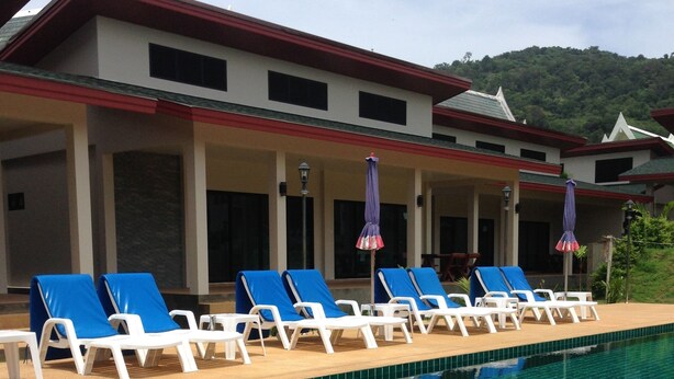 A poolside area with lounge chairs and umbrellas, a covered seating area, and a view of a mountainous landscape. - Naya Pool Villa (Rawai)