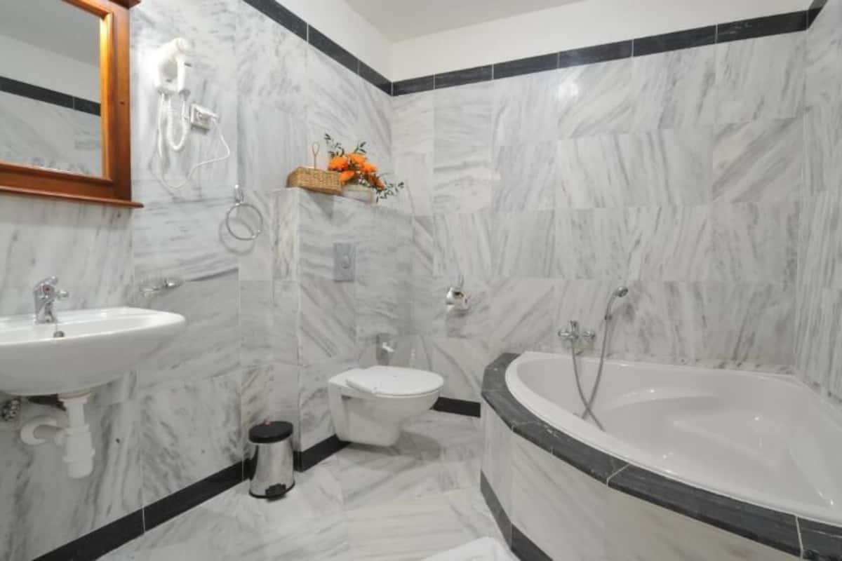 A bathroom with a white sink, toilet, and bathtub, marble walls, and a wooden-framed mirror.