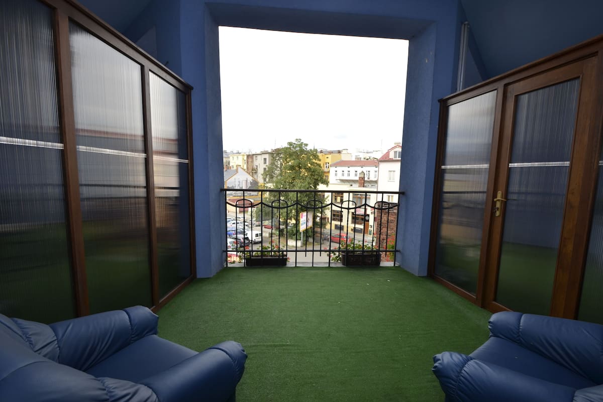 A balcony with artificial grass, two blue sofas, and a view of buildings and a street.