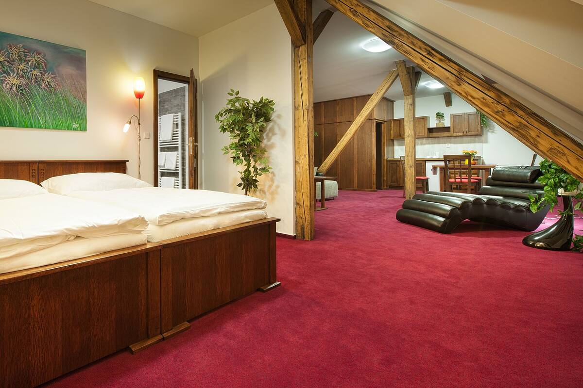 A bedroom with a wooden bed, red carpet, and a view of a kitchen and dining area.