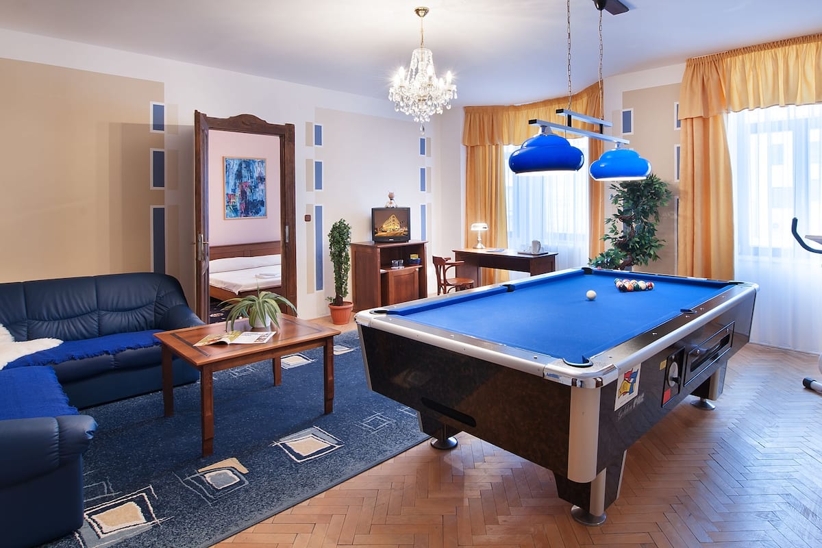 A living room with a pool table, a blue sofa, a coffee table, and a treadmill.