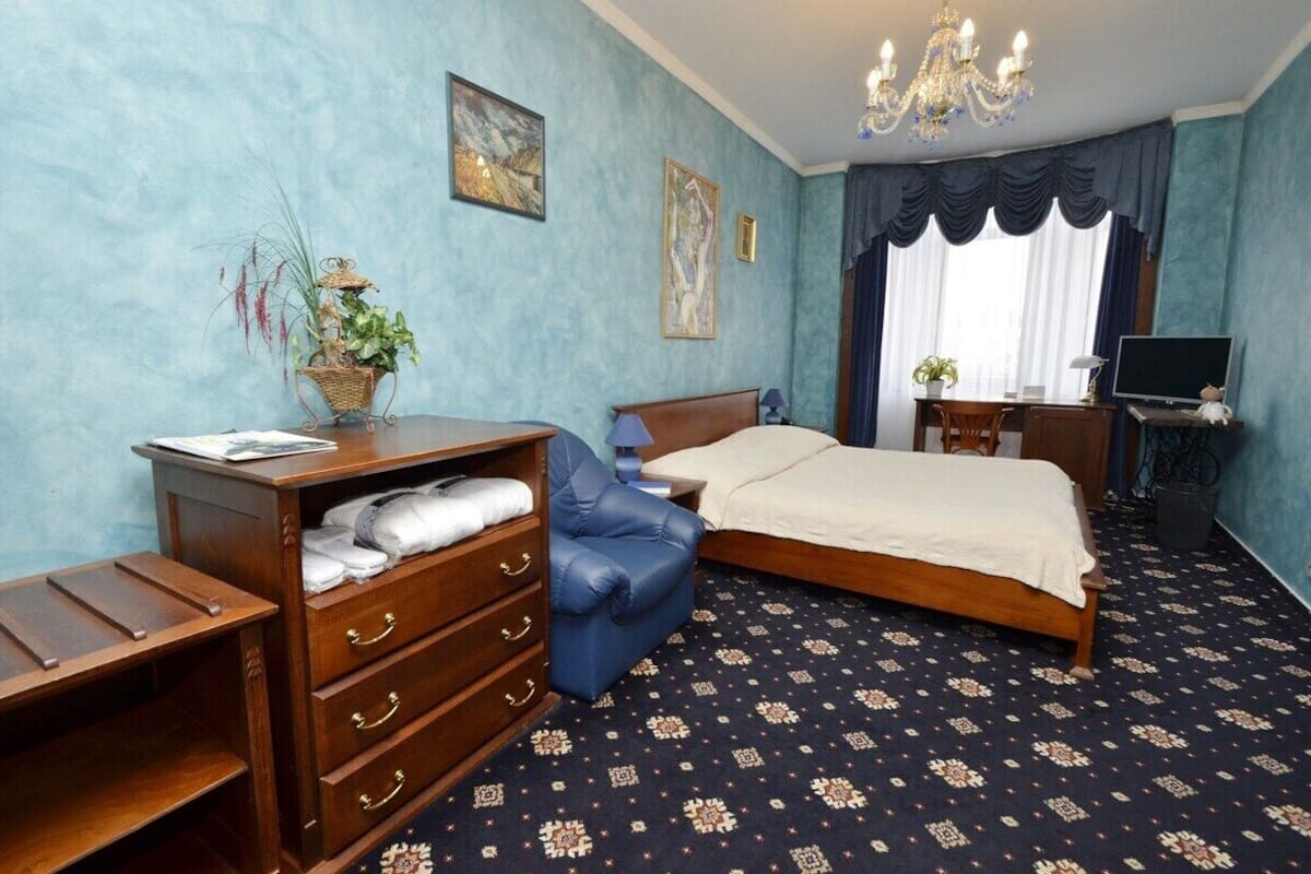 A bedroom with a bed, a desk, a chair, a television, and a window with curtains.