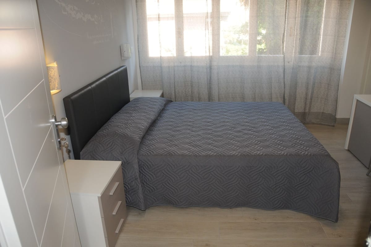 Een slaapkamer met een bed, nachtkastje, lamp en een raam met gordijnen.