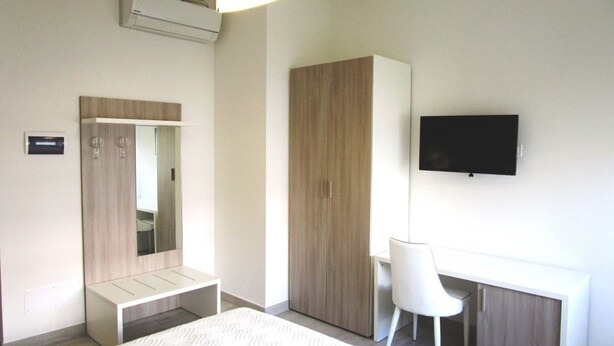A modern hotel room with a bed, a desk, a chair, a wardrobe, a television, and an air conditioning unit. - La Perla Affittacamere (La Spezia)