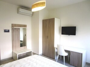 Habitación de hotel moderna con cama, escritorio, silla, armario, televisor y aire acondicionado.