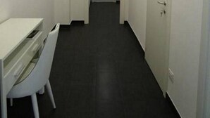 A narrow hallway with a white desk and chair on the left, a door at the end, and a door on the right. - La Perla Affittacamere (La Spezia)