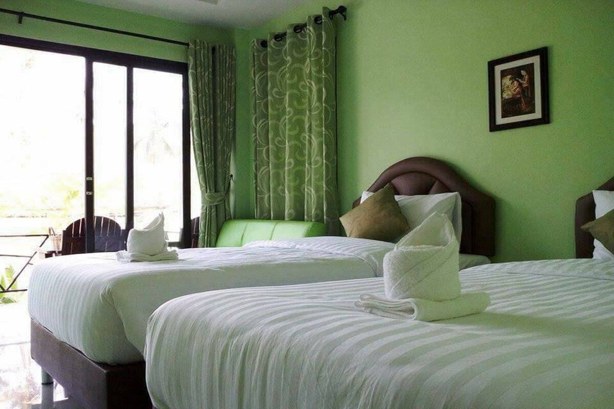 Ein Hotelzimmer mit zwei Betten, grünen Vorhängen, einem gerahmten Bild an der Wand und Blick aus dem Fenster.
