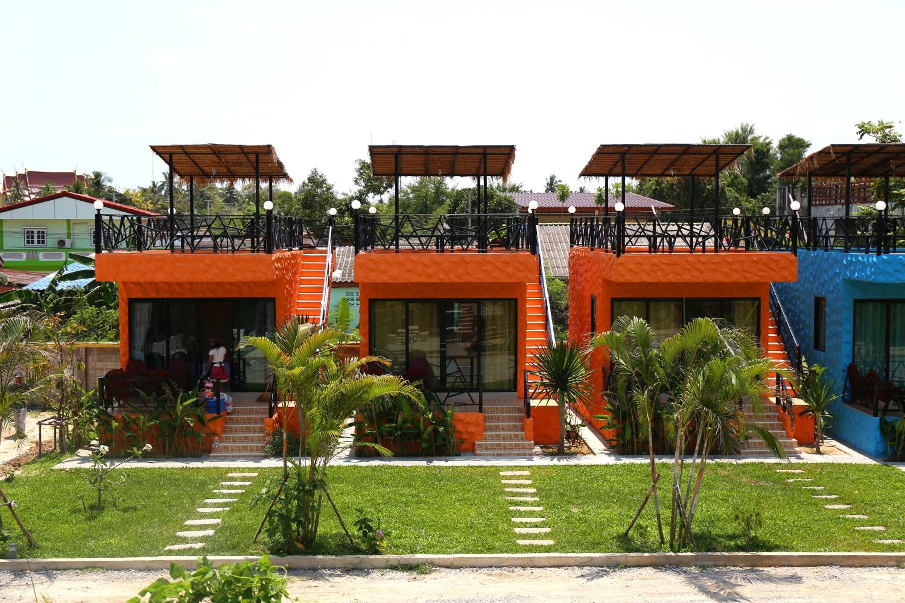 A hotel with two orange buildings, each with a covered outdoor seating area and a staircase leading to the entrance.