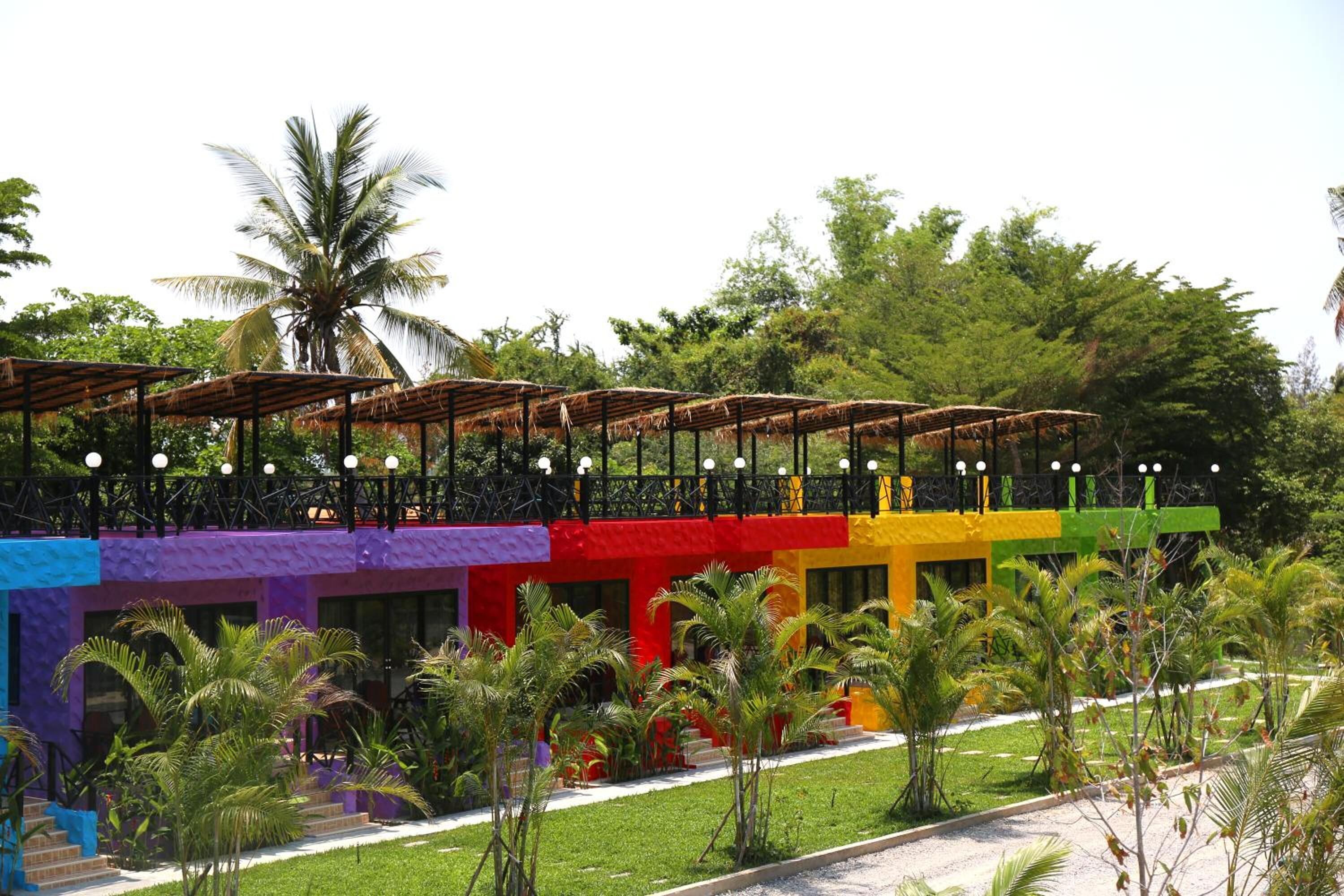 A multi-story building with colorful facades, a covered outdoor seating area, and a well-maintained garden with palm trees.
