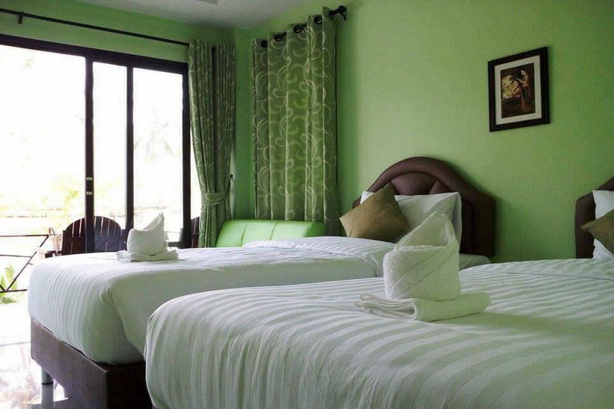 Ein Hotelzimmer mit zwei Betten, grünen Vorhängen und einem gerahmten Bild an der Wand.