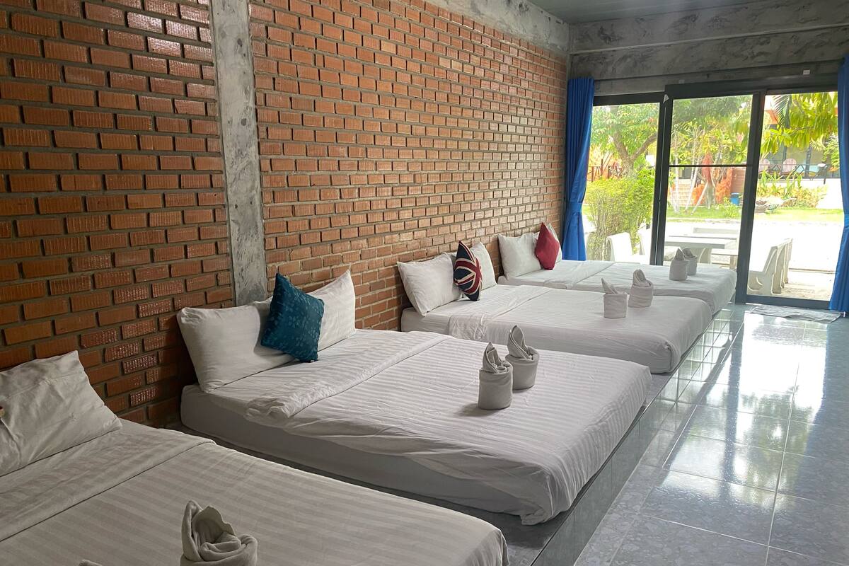 Ein Hotelzimmer mit vier Betten, jeweils mit weißer Bettwäsche und Kissen, einer Ziegelwand und Blick ins Freie.