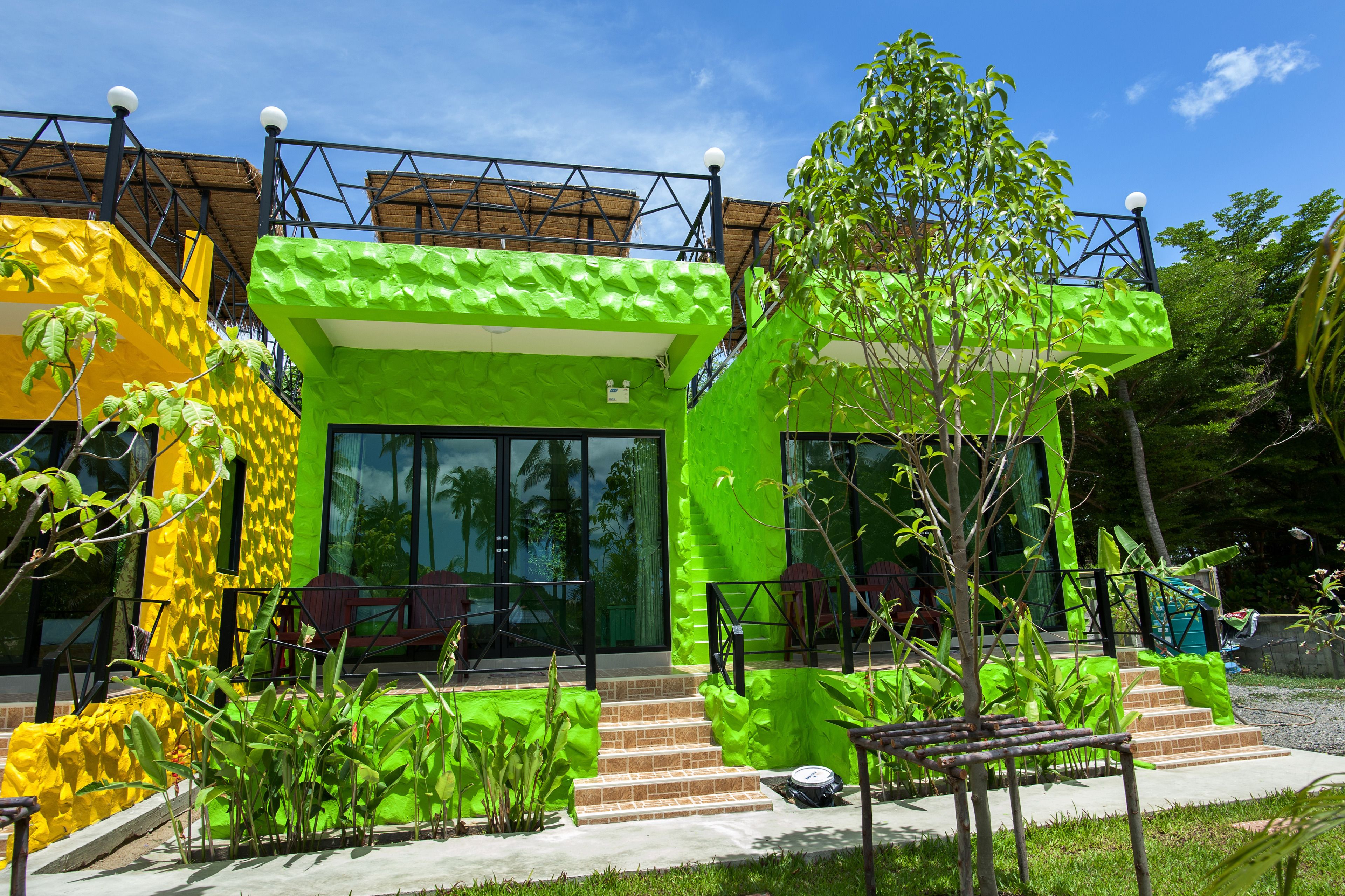 A modern building with a green exterior, large windows, and a staircase leading to the entrance.