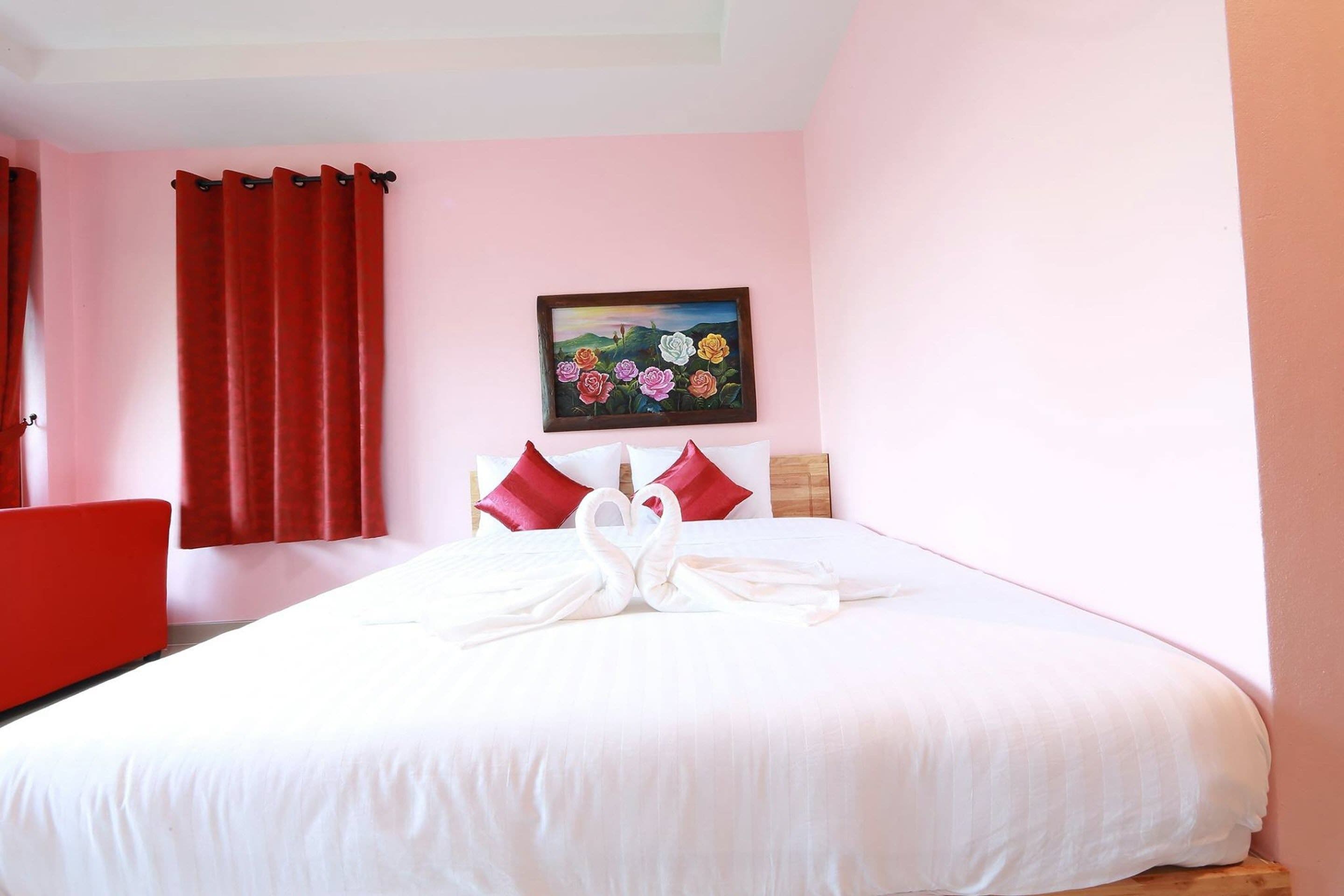 Une chambre d’hôtel avec un grand lit, des rideaux rouges, un tableau au mur et un fauteuil rouge.