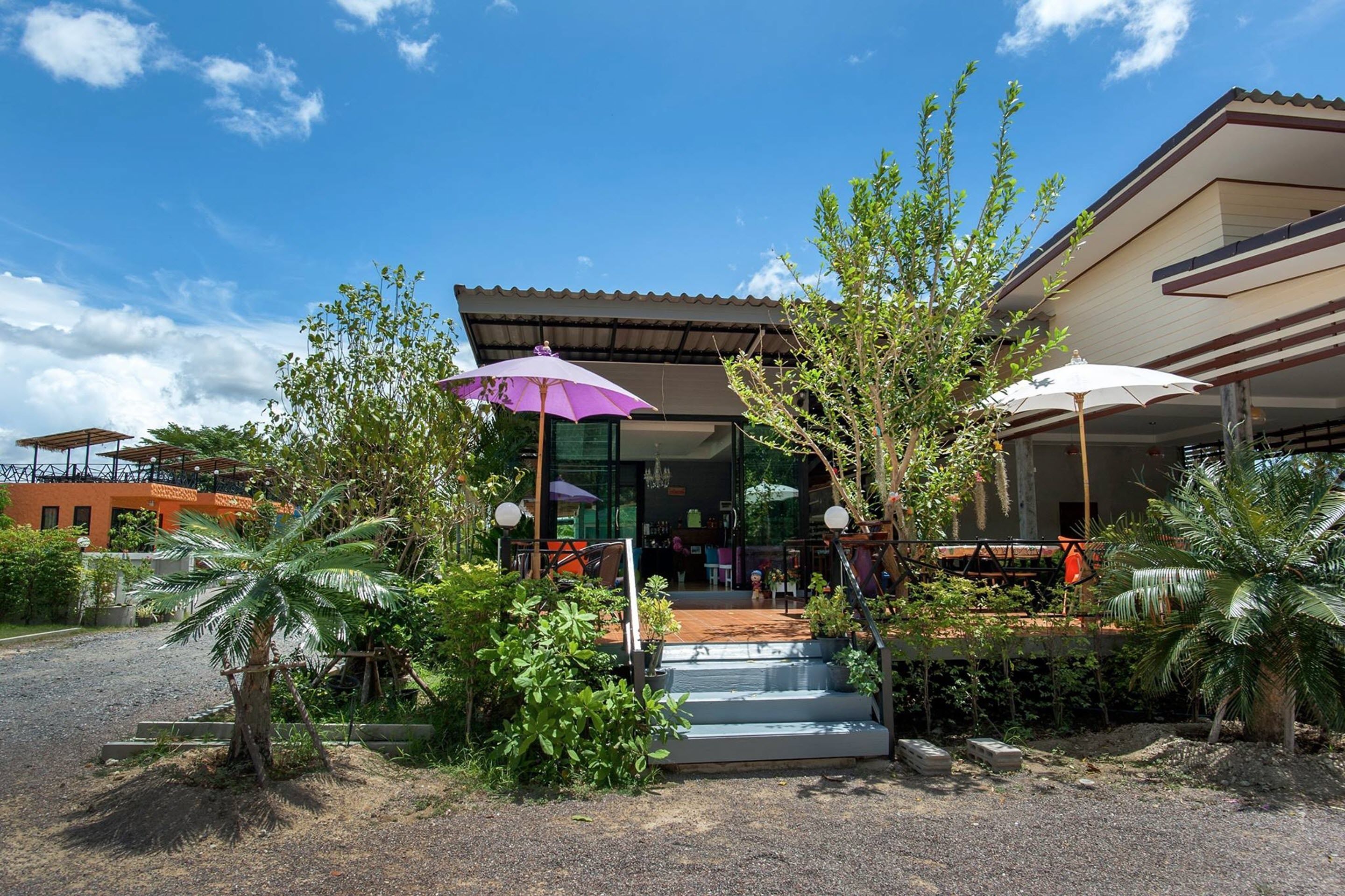 A building with a covered entrance, outdoor seating, and palm trees.