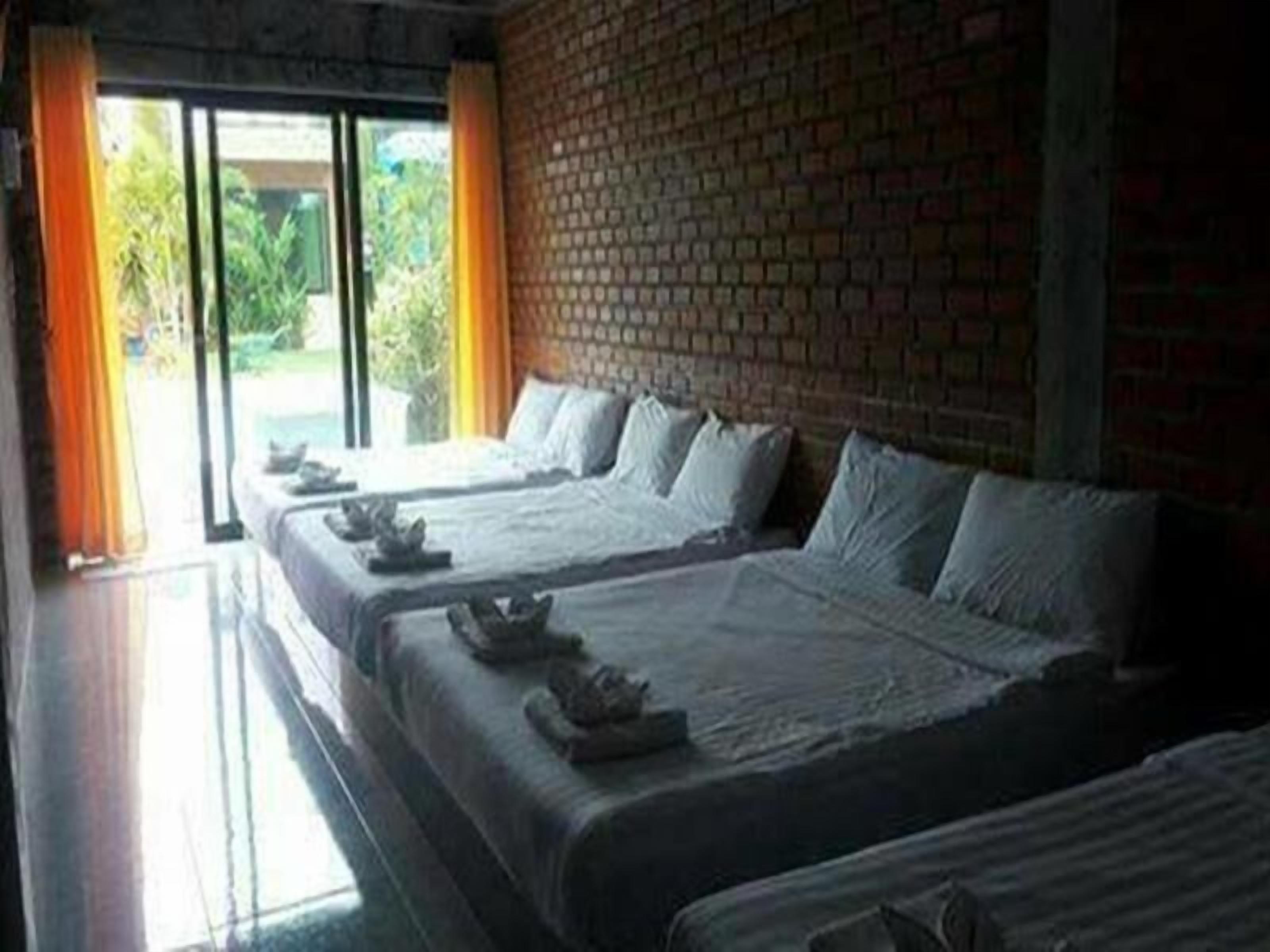 A hotel room with two beds, a brick wall, and a view of greenery outside.