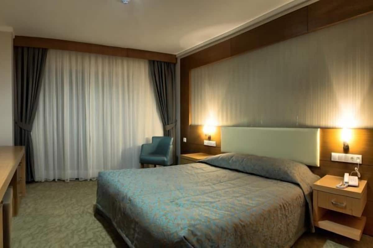 A hotel room with a bed, a desk, a chair, and a TV.