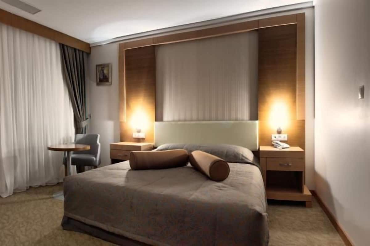 A hotel room with a large bed, two bedside tables with lamps, a small round table, and a chair.