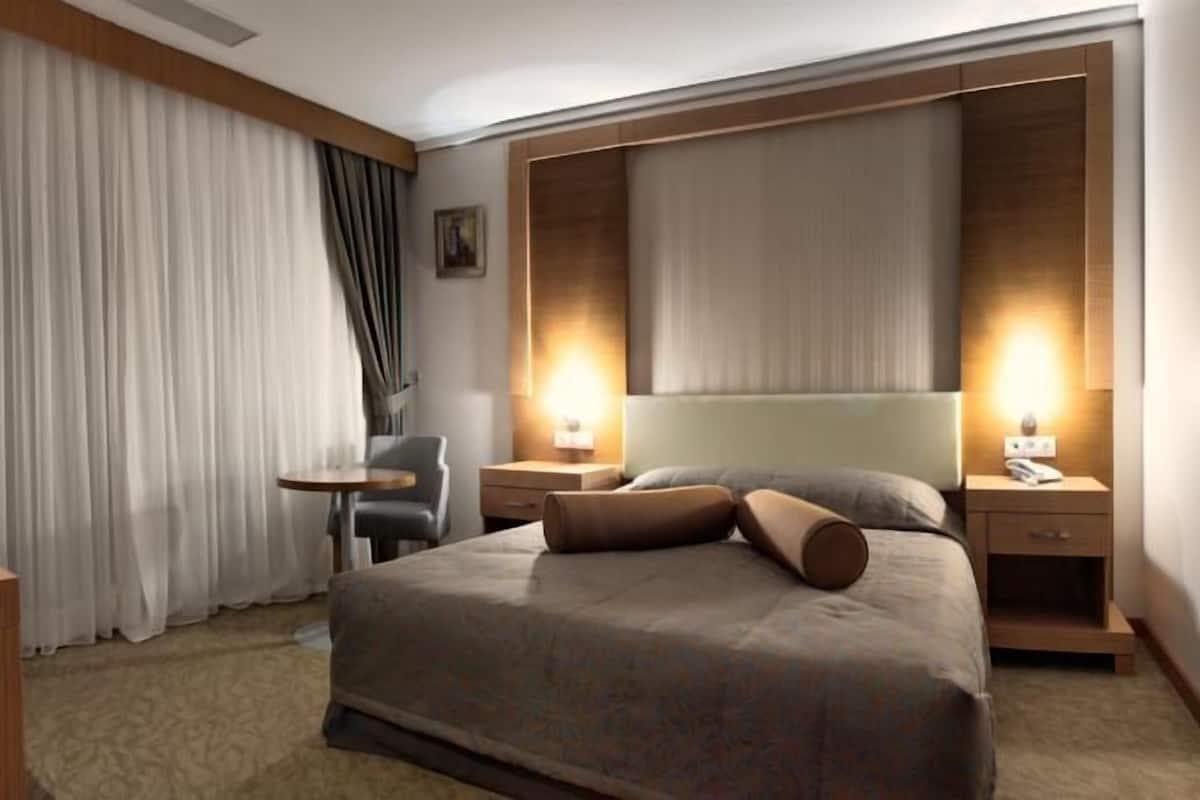 A hotel room with a large bed, two bedside tables, a chair, and a desk.