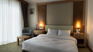 A hotel room with a large bed, two bedside tables, a chair, and a nightstand with a lamp. - Buyuk Anadolu Eregli Hotel (Karadeniz Eregli)