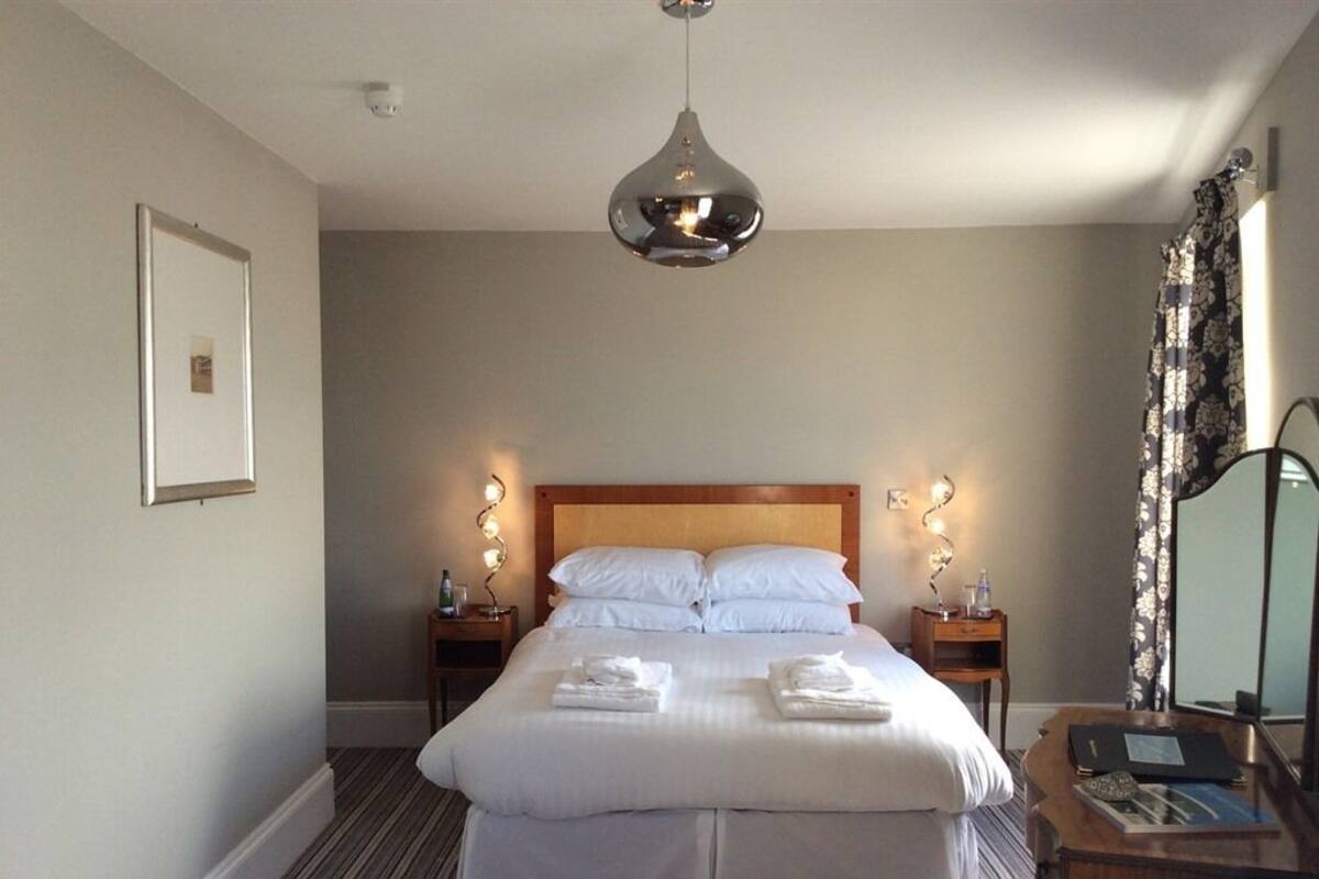 A neatly made bed with white linens, two bedside tables with lamps, a wooden headboard, and a hanging pendant light.