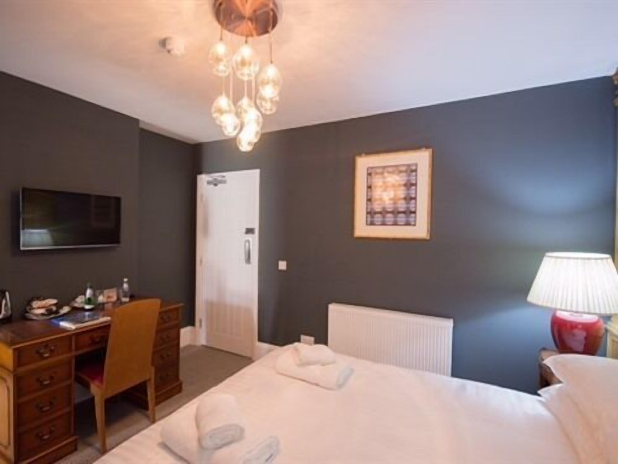 A hotel room with a bed, a desk, a chair, a television, a framed picture, and a lamp.