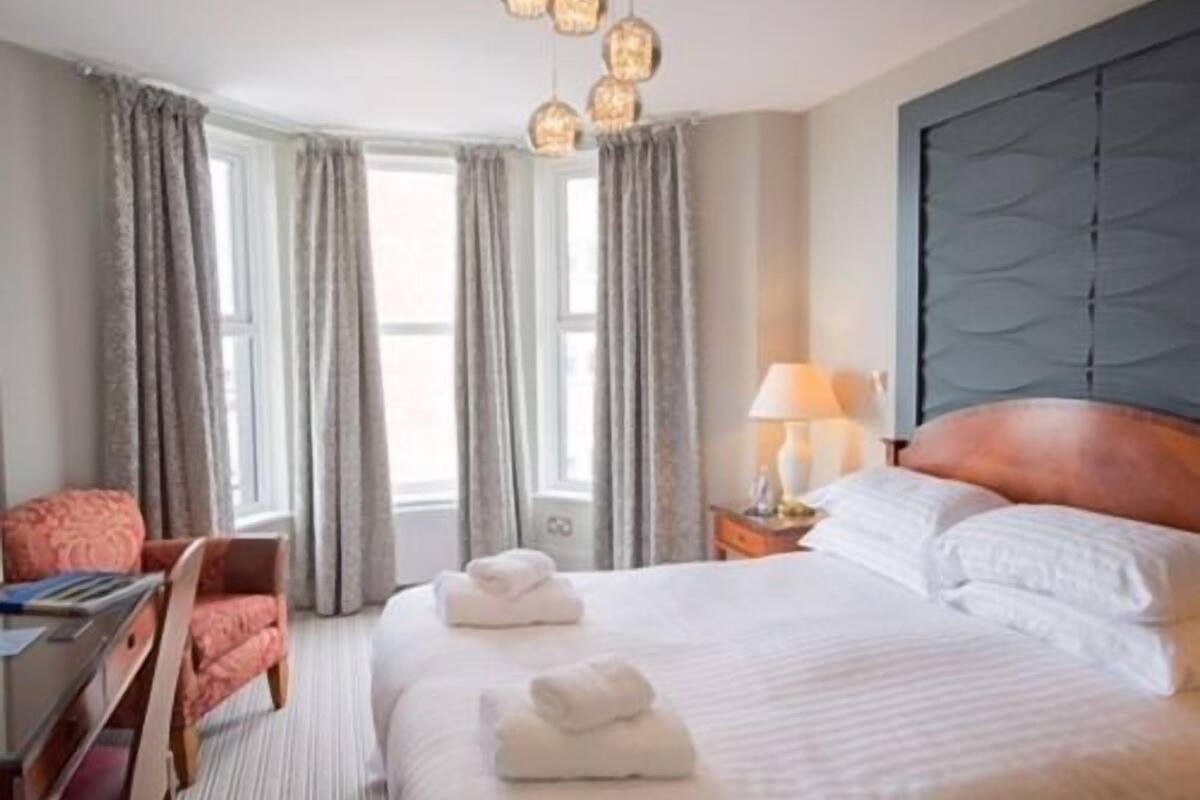 A hotel room with a bed, a desk, a chair, and a lamp.