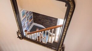A mirror with an ornate frame reflecting a staircase with a wooden handrail and a railing.