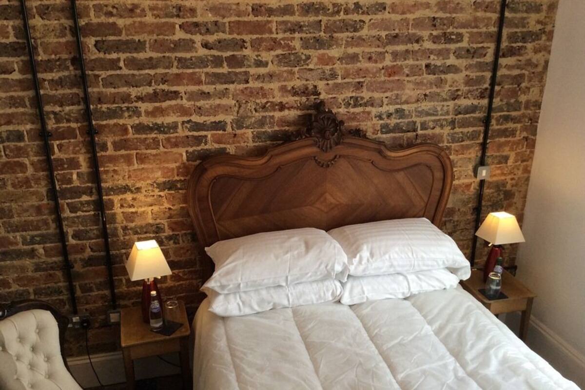 A bed with a wooden headboard, two bedside lamps, and a brick wall in the background.