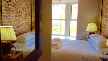 A hotel room with a brick wall, a large bed with white linens, two bedside lamps, and a chandelier.