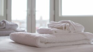 A stack of white towels on a bed in a room with large windows.