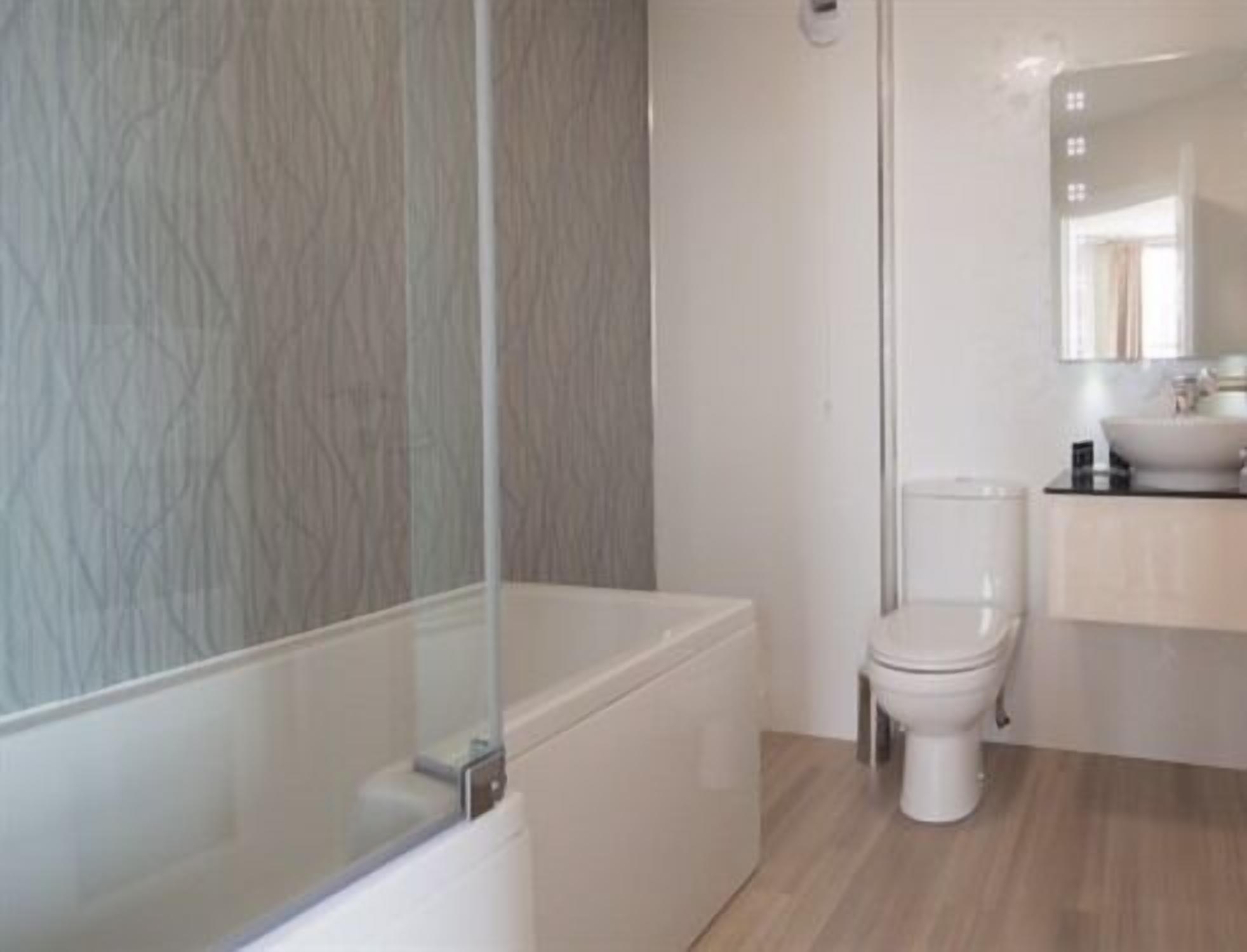 A modern bathroom with a glass shower enclosure, a white toilet, and a sink with a mirror above it.