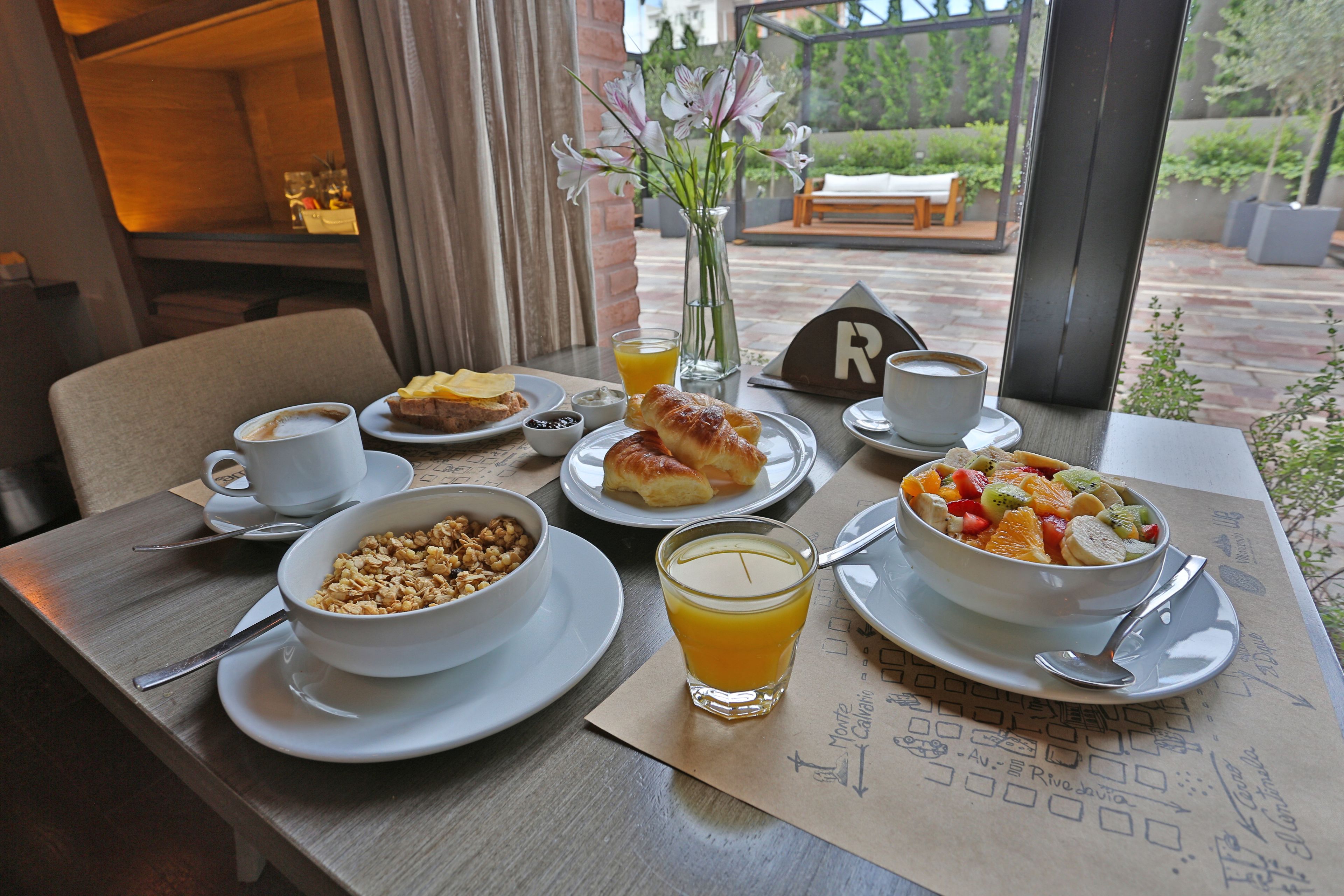Una tavola imbandita con piatti di cibo, un bicchiere di succo d'arancia e un vaso di fiori.