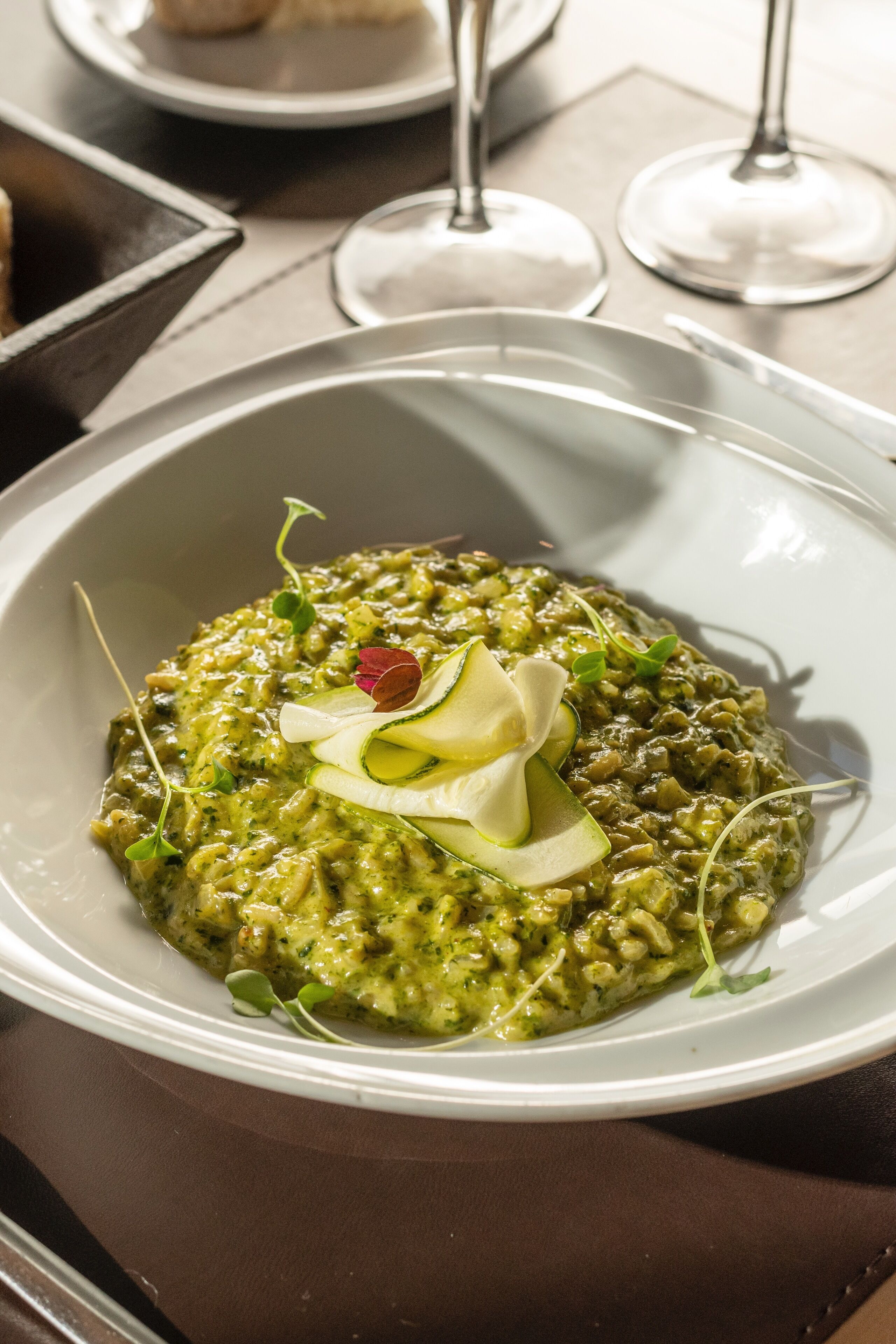Eine Schüssel grüner Risotto, garniert mit Mikrogrün und einem Klecks Sahne, auf einem weißen Teller.