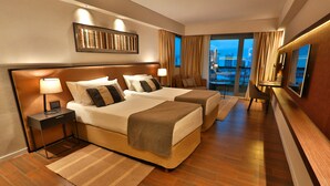 Habitación de hotel con dos camas, un ventanal con vistas, un televisor de pantalla plana y un escritorio con lámpara.