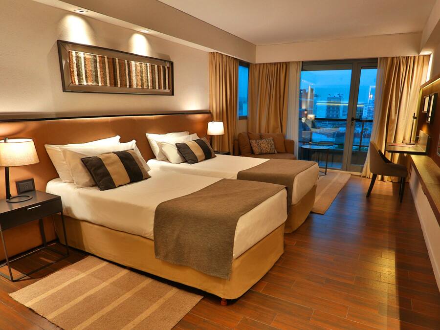 A hotel room with two beds, a large window with a view, a flat-screen TV, and a desk with a lamp.
