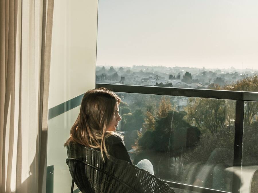 Una persona sentada en una silla junto a una ventana con vistas a un paisaje urbano.