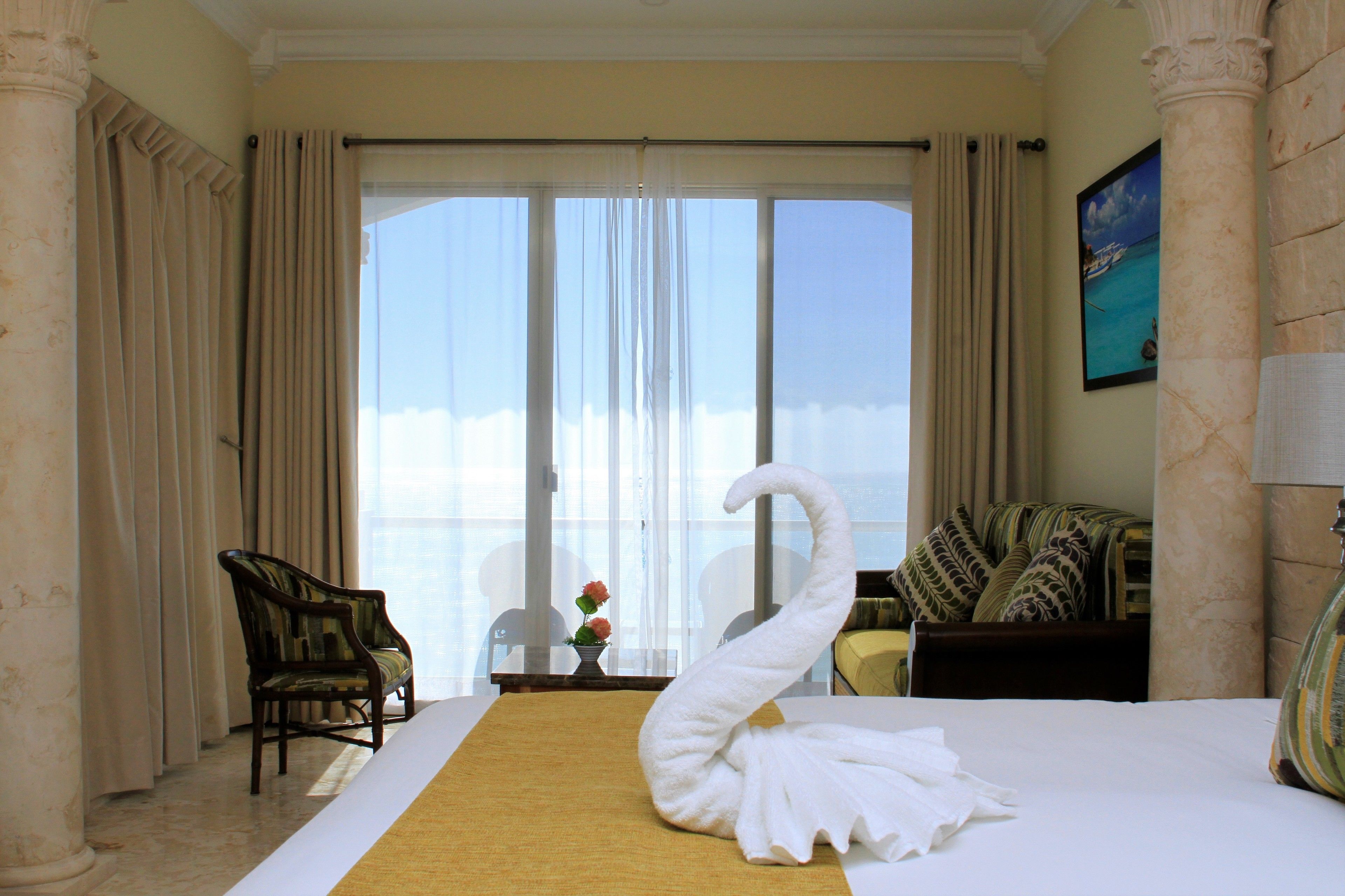 Hotelkamer met een groot bed, een handdoek in de vorm van een zwaan, uitzicht op zee door het raam, en een stoel bij het raam.