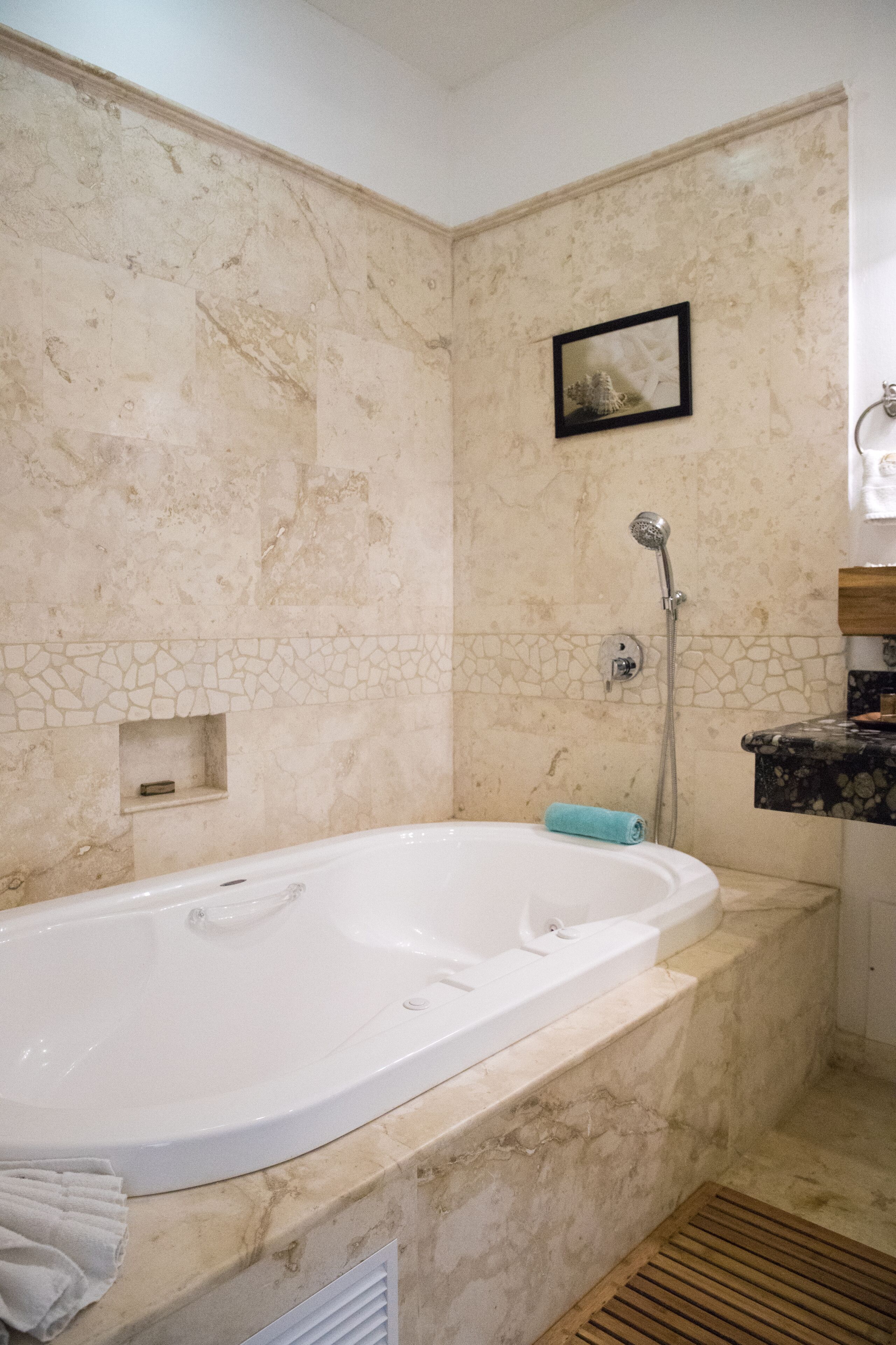 Un baño con una bañera grande, ducha y un estante pequeño con un cuadro enmarcado.