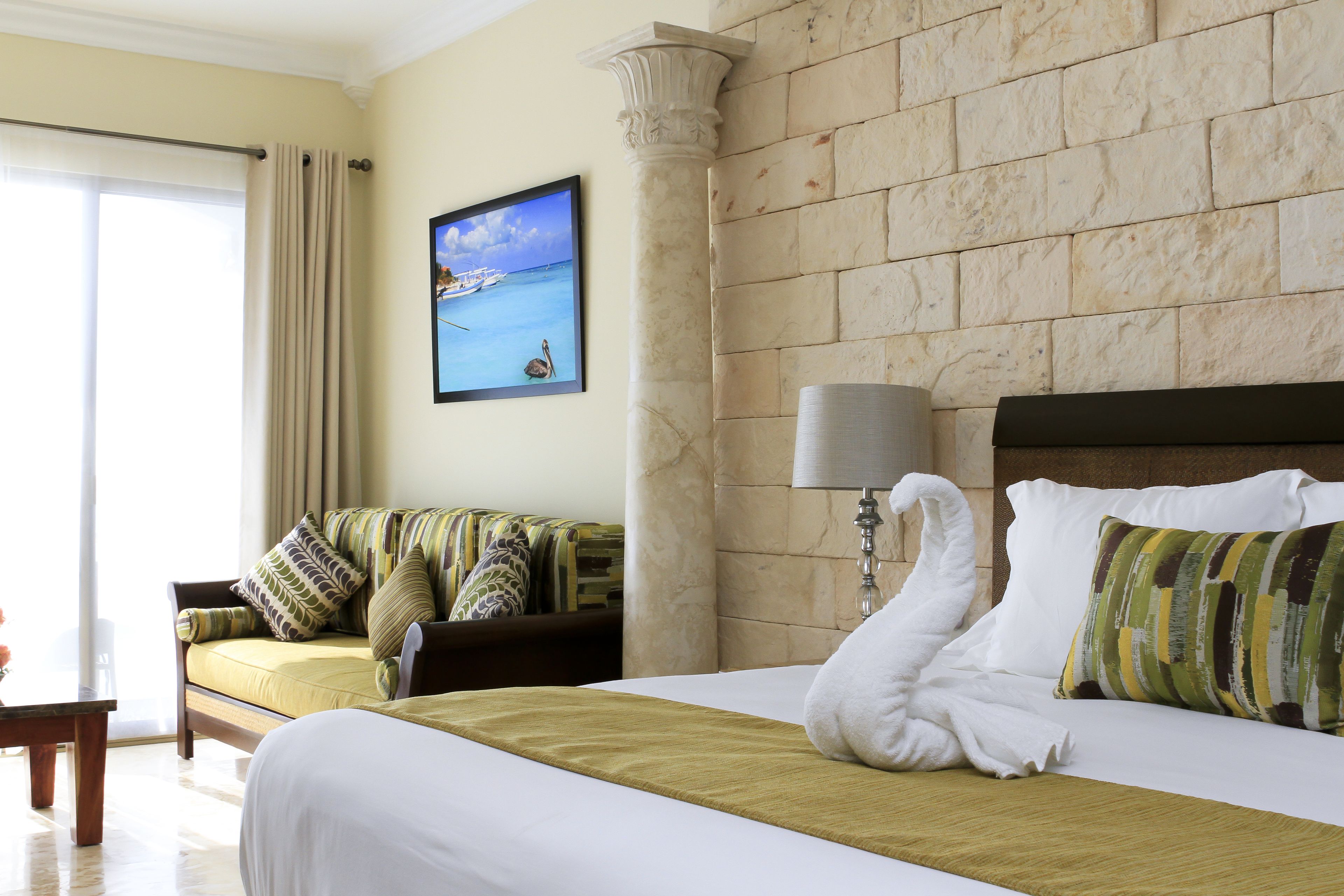 A hotel room with a bed, a sofa, a lamp, and a painting of a boat on the wall.