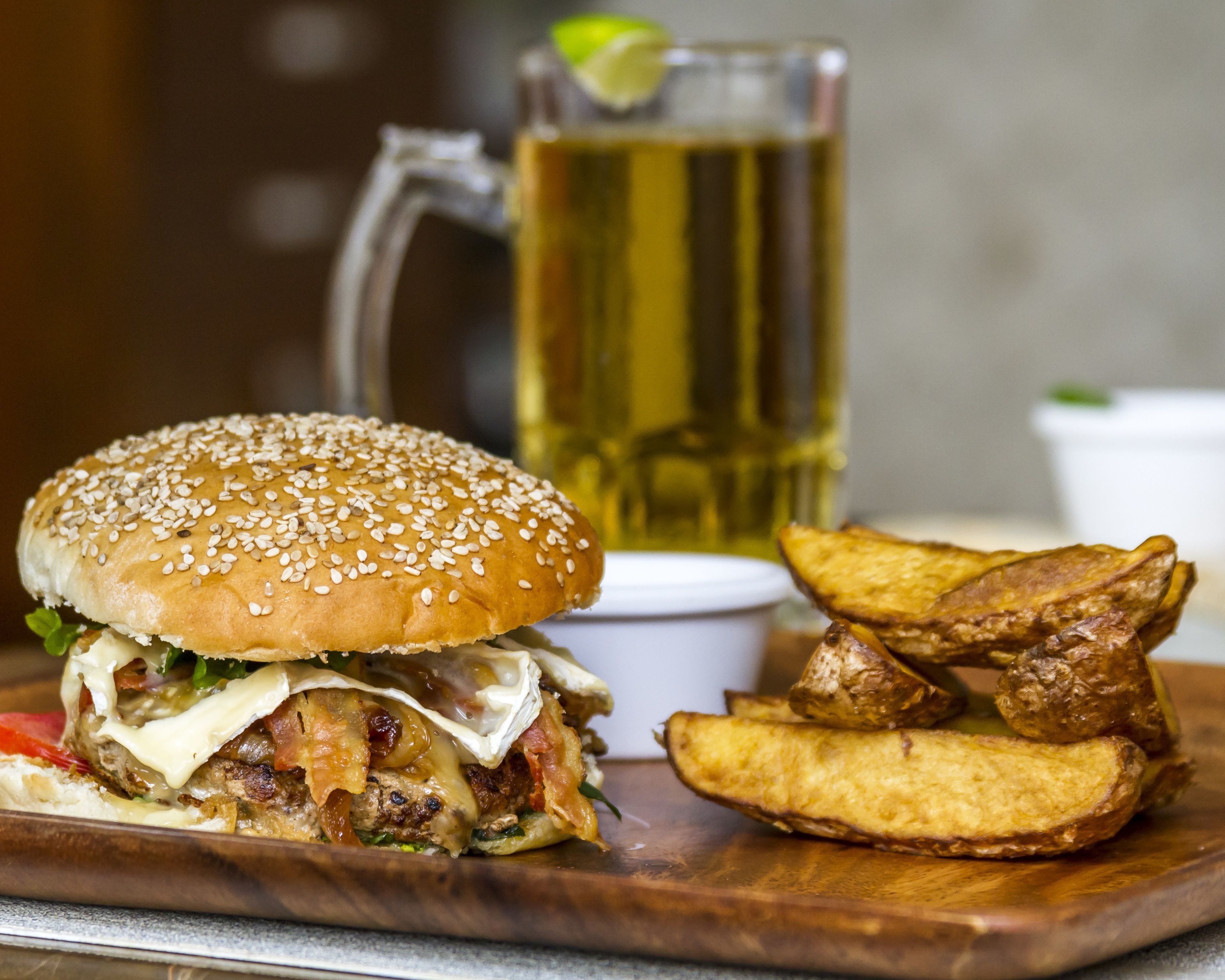 A burger with fries and a drink on a wooden board.