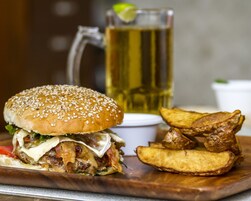 A burger with fries and a drink on a wooden board.