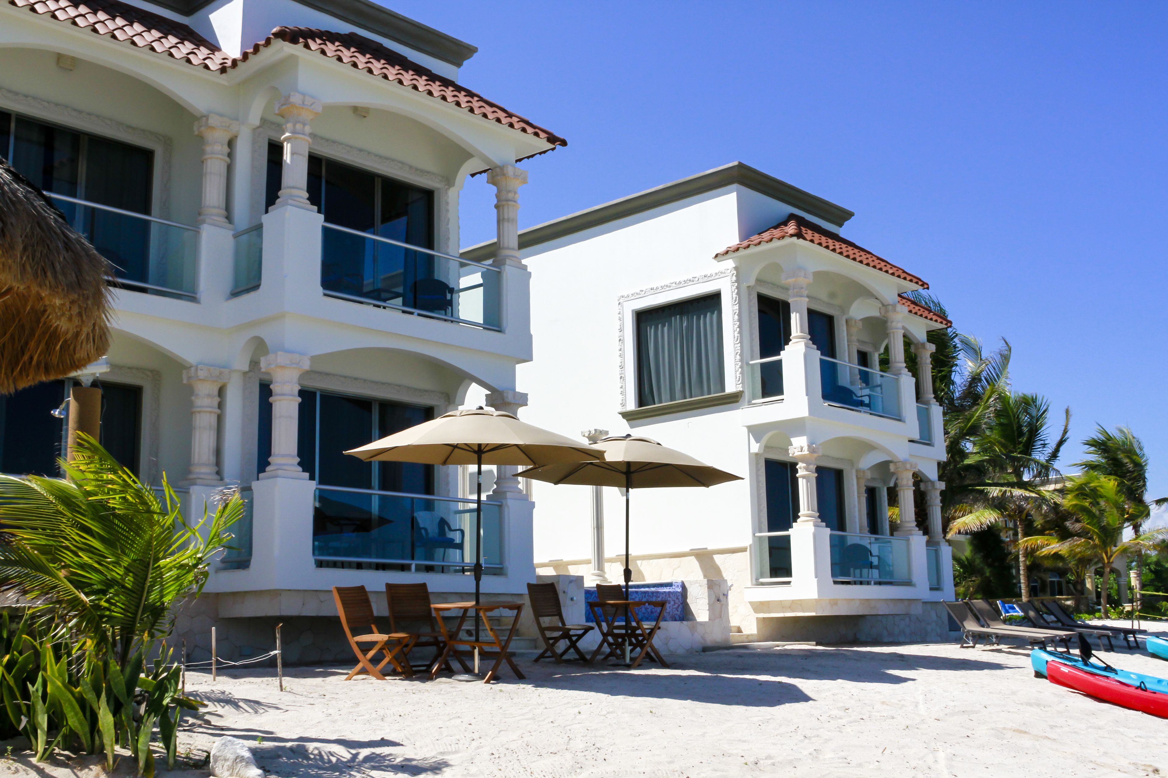 A beachfront property with a white building, outdoor seating, and a red kayak.