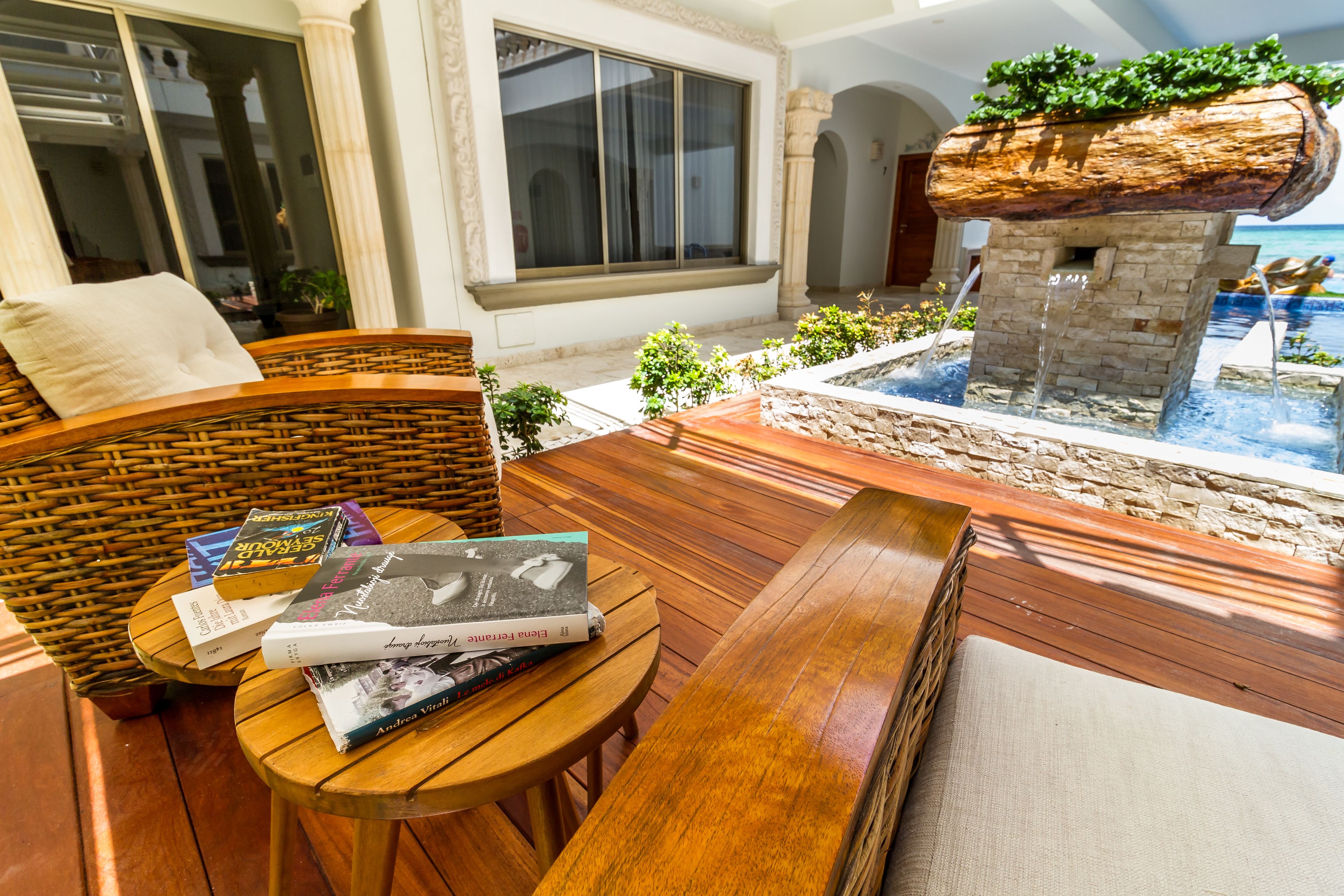 A wooden deck with a wicker chair, a small round table with books, and a stone fountain.